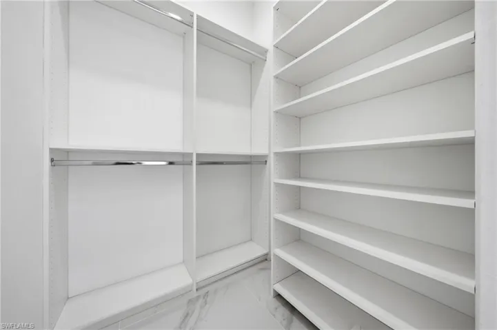 Expansive walk-in closet featuring custom white built-in shelving, chrome hanging rods, and light-toned tile flooring