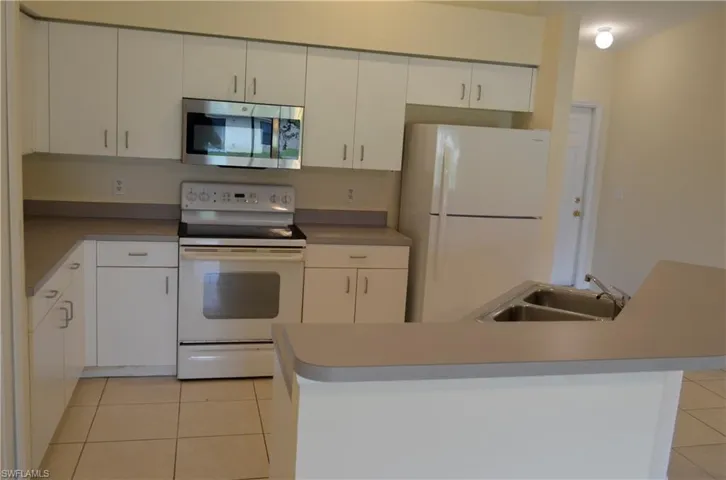 Kitchen featuring white appliances, light tile patterned floors, white cabinetry, and an island with sink