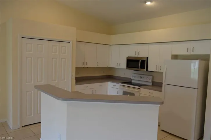 Kitchen featuring white appliances, light tile patterned flooring, white cabinets, vaulted ceiling, and a center island