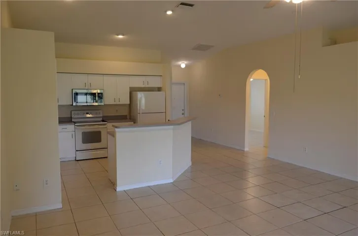 Kitchen featuring arched walkways, white appliances, white cabinetry, light tile patterned floors, and a ceiling fan