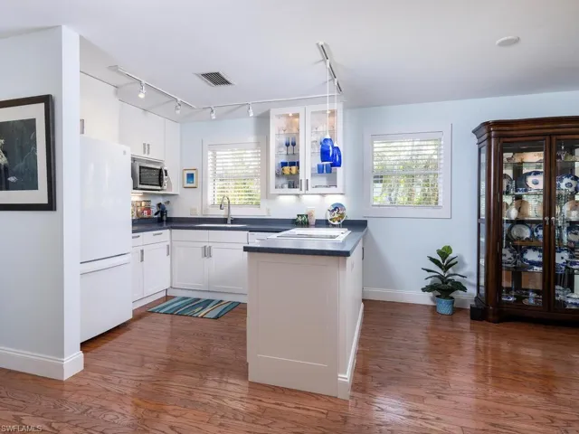 Kitchen featuring a peninsula, stainless steel microwave, dark countertops, a sink, and freestanding refrigerator