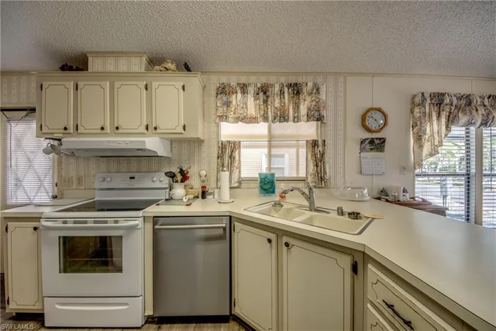 Kitchen with cream cabinets, white range with electric stovetop, light countertops, dishwasher, and a textured ceiling