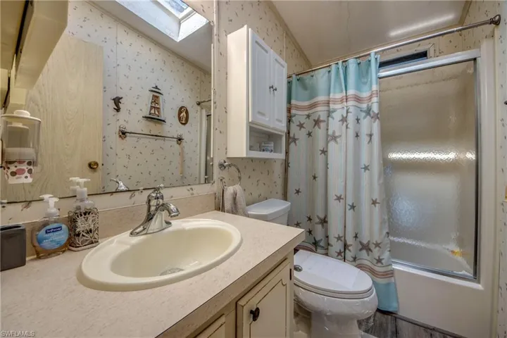 Bathroom featuring wallpapered walls, a skylight, vanity, and shower / bathtub combination with curtain