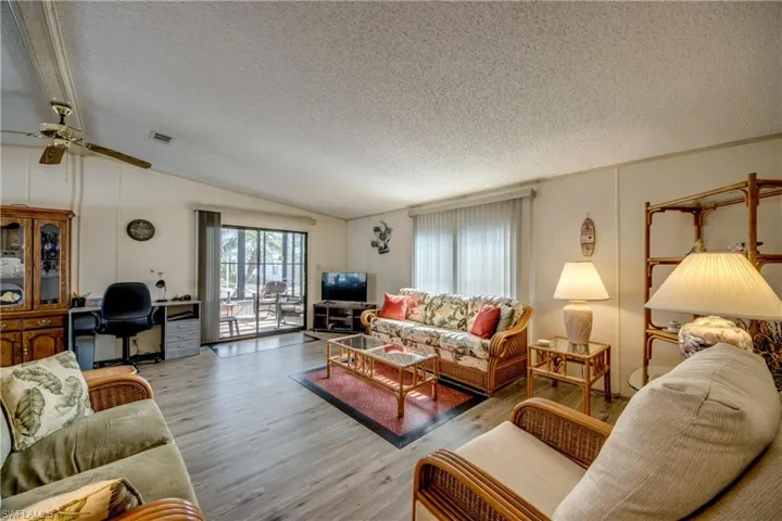 Living room featuring lofted ceiling, wood finished floors, a textured ceiling, a ceiling fan, and a desk