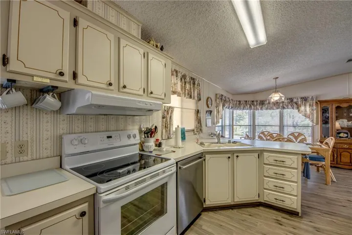 Kitchen with white range with electric cooktop, cream cabinetry, light countertops, a peninsula, and vaulted ceiling