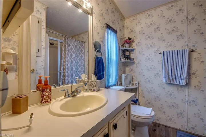 Full bathroom featuring curtained shower, wallpapered walls, a textured ceiling, vanity, and wood finished floors