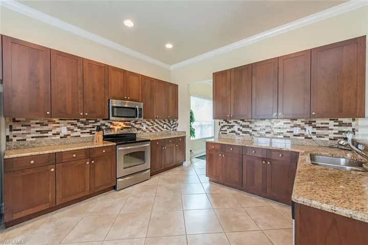 Kitchen with appliances with stainless steel finishes, light stone counters, ornamental molding, light tile patterned floors, and tasteful backsplash