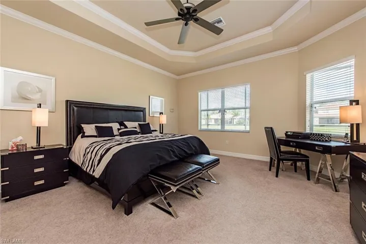 Bedroom with light carpet, ornamental molding, a raised ceiling, and a ceiling fan