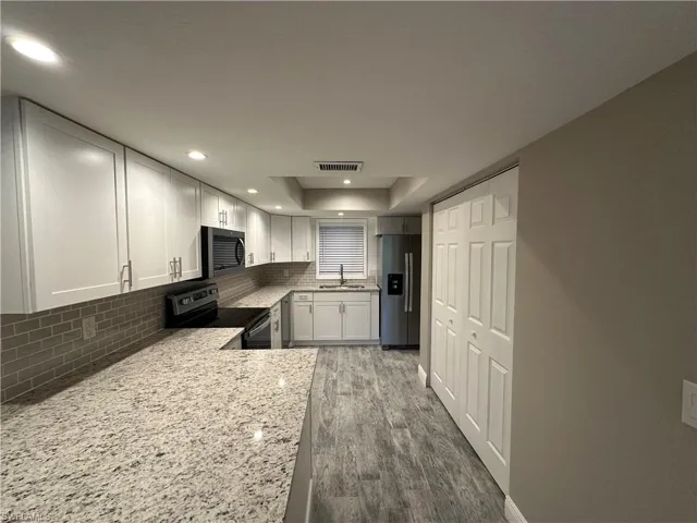 Kitchen featuring decorative backsplash, appliances with stainless steel finishes, white cabinets, light stone counters, and dark wood-type flooring