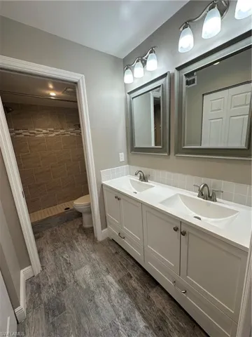 Full bathroom featuring a shower stall, double vanity, and dark wood-style flooring