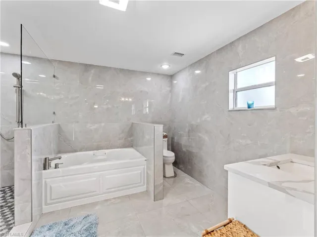 Bathroom with tile walls, vanity, a garden tub, a marble finish shower, and light tile patterned flooring