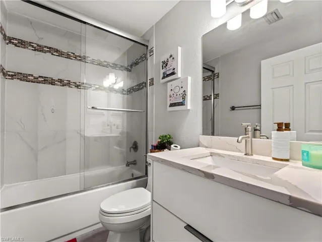 Full bathroom with a textured wall, combined bath / shower with glass door, and vanity
