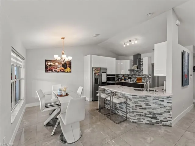 Kitchen with white cabinetry, decorative backsplash, lofted ceiling, a peninsula, and wall chimney exhaust hood