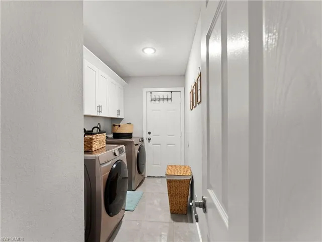 Washroom with light tile patterned floors, cabinet space, separate washer and dryer, and a textured wall