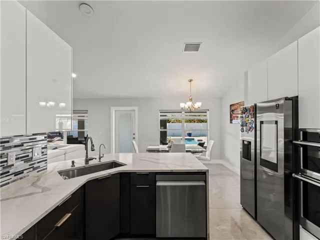 Kitchen featuring a chandelier, modern cabinets, stainless steel appliances, light stone counters, and recessed lighting