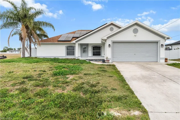 Single story home with solar panels, stucco siding, driveway, an attached garage, and a front yard