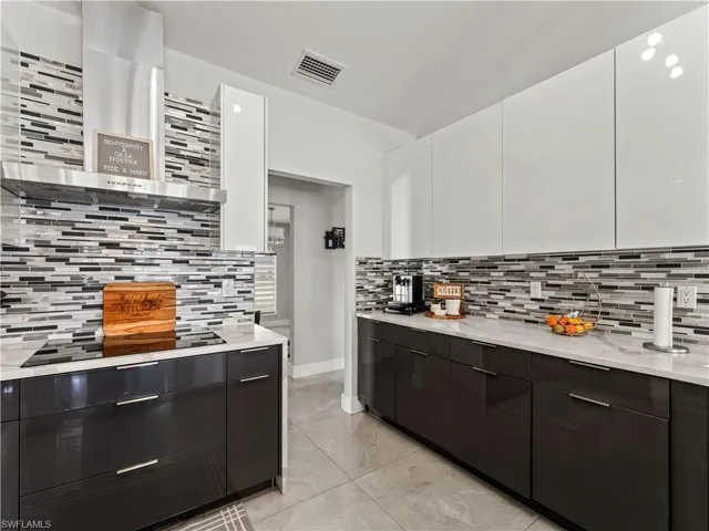 Kitchen featuring modern cabinets, white cabinets, tasteful backsplash, and wall chimney range hood