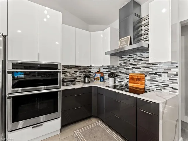 Kitchen with white cabinets, stainless steel double oven, modern cabinets, and wall chimney range hood