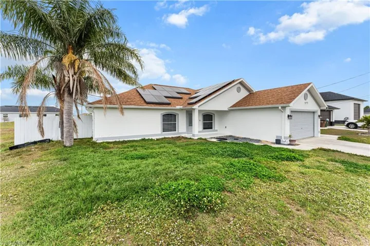 View of front of home with a garage, solar panels, stucco siding, driveway, and a shingled roof