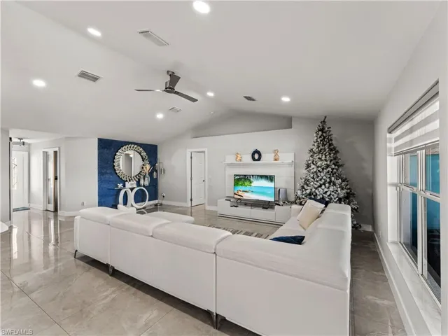 Living room featuring lofted ceiling, ceiling fan, recessed lighting, light marble finish floors, and a fireplace