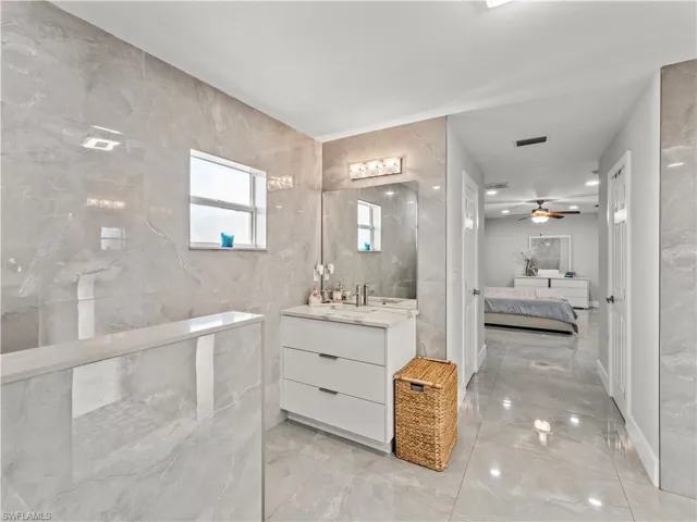Ensuite bathroom featuring vanity, light marble finish floors, tile walls, and ceiling fan