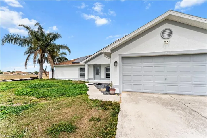 Ranch-style home with stucco siding, solar panels, driveway, a garage, and a front yard
