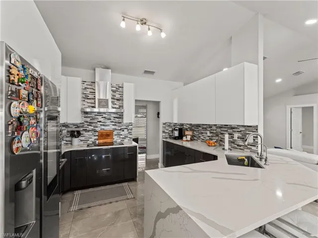 Kitchen with white cabinets, a peninsula, light stone counters, decorative backsplash, and dark cabinetry