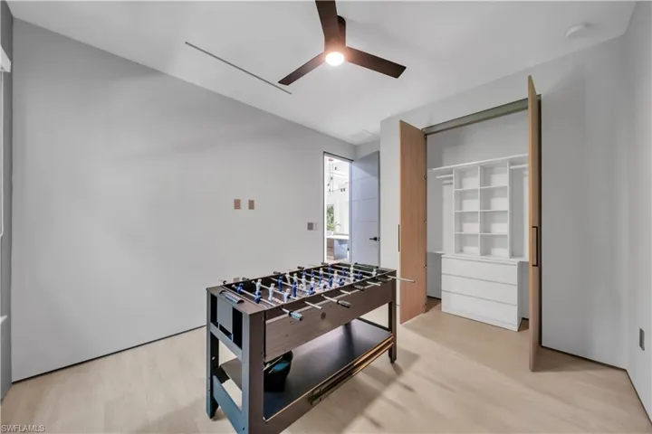 Room featuring light wood-finish flooring, a modern ceiling fan, and a built-in closet system with shelving and drawers