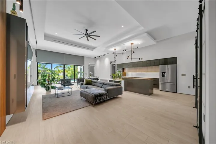Expansive open-concept living space featuring light wood-finish flooring, a contemporary kitchen with stainless steel appliances, and a recessed ceiling with integrated lighting
