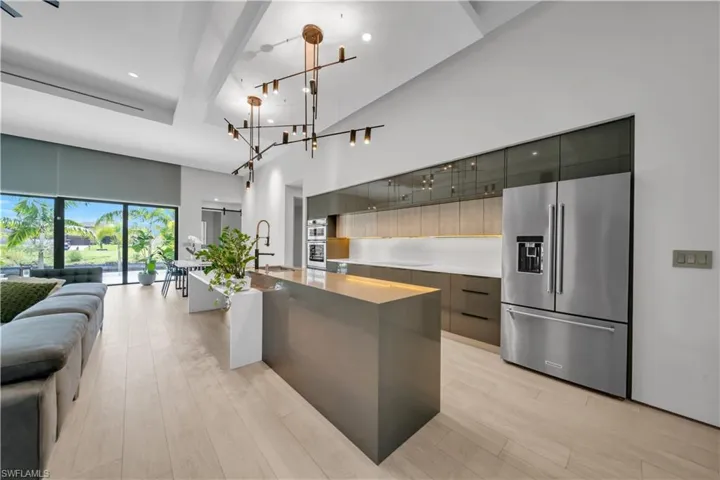 Modern kitchen featuring a large waterfall island, stainless steel refrigerator, integrated double ovens, and a contemporary chandelier
