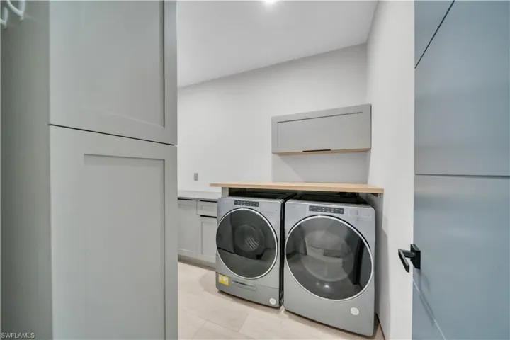 Dedicated laundry space featuring stacked appliances, light wood-finish countertop, and ample built-in cabinetry with shaker-style doors