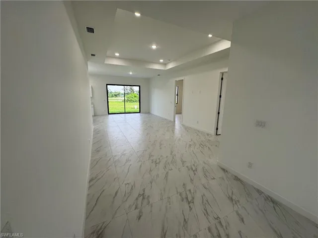 Unfurnished room with a raised ceiling, recessed lighting, and light marble finish floors