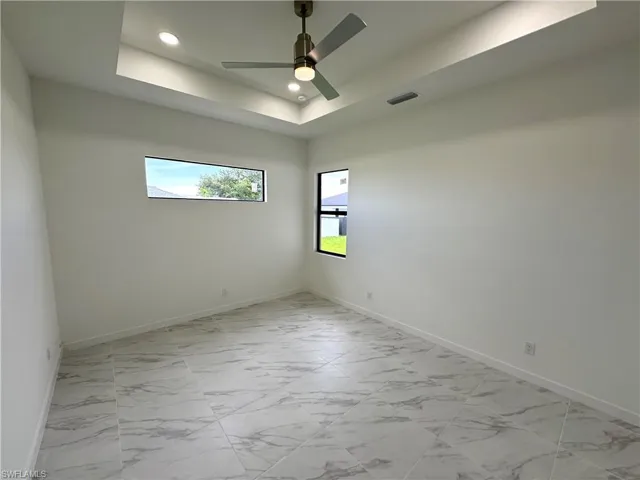 Spare room featuring light marble finish flooring, a raised ceiling, recessed lighting, and a ceiling fan
