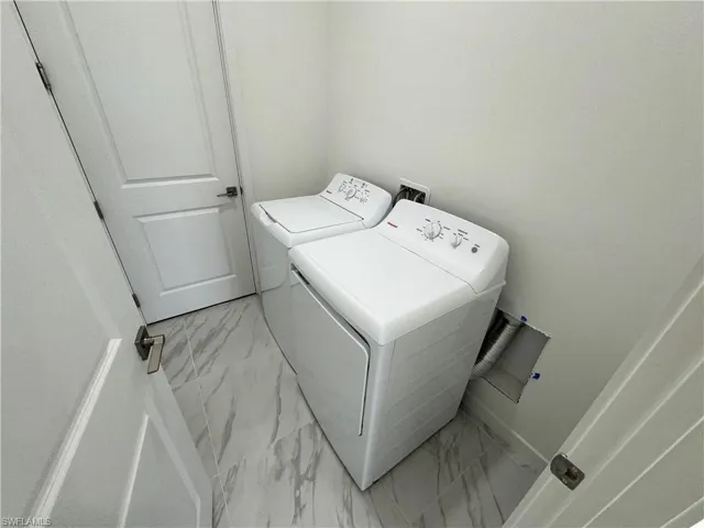 Laundry area featuring light marble finish flooring and separate washer and dryer