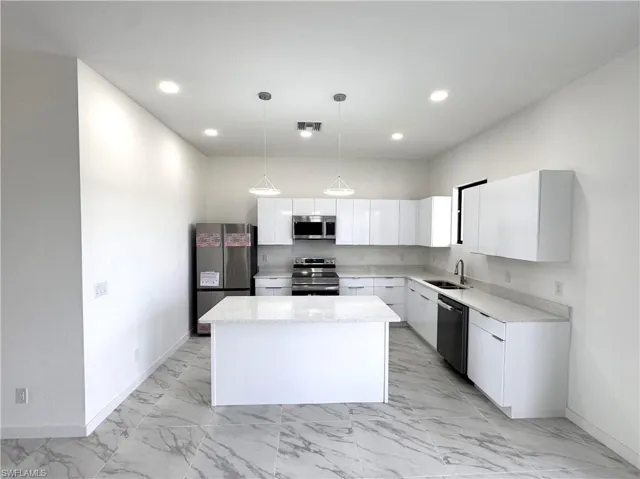 Kitchen featuring white cabinetry, appliances with stainless steel finishes, a kitchen island, pendant lighting, and light stone counters