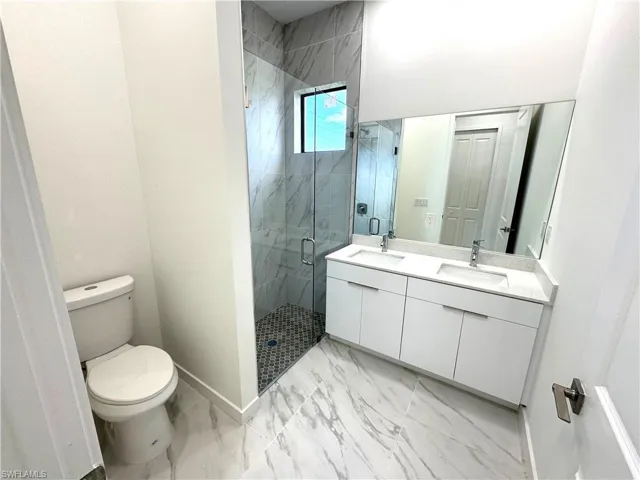Bathroom with a marble finish shower, double vanity, and light marble finish floors