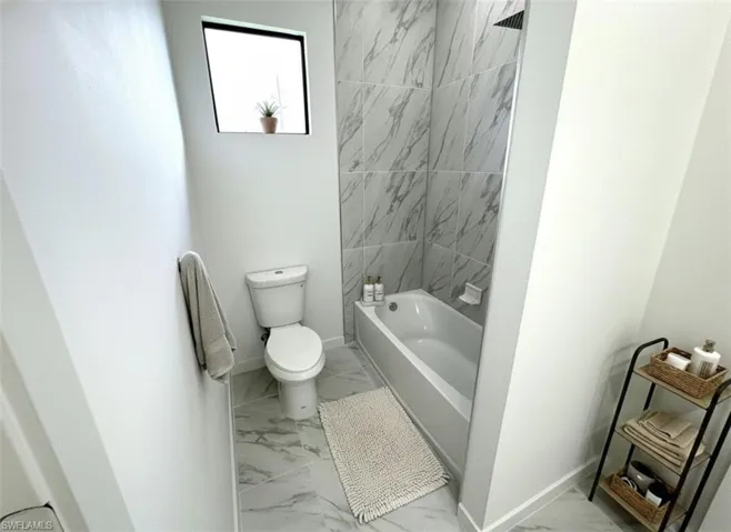 Bathroom featuring light marble finish floors and tub / shower combination