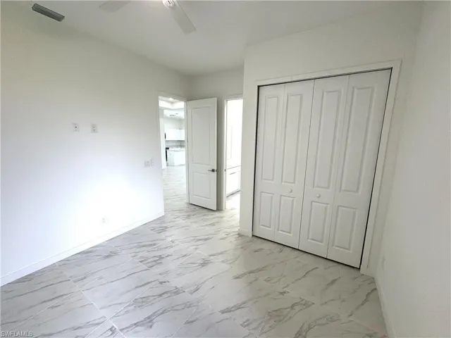 Unfurnished bedroom featuring light marble finish floors, a ceiling fan, and a closet