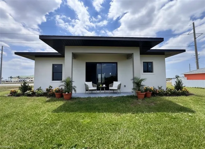 Back of house with stucco siding, a patio, and a lawn