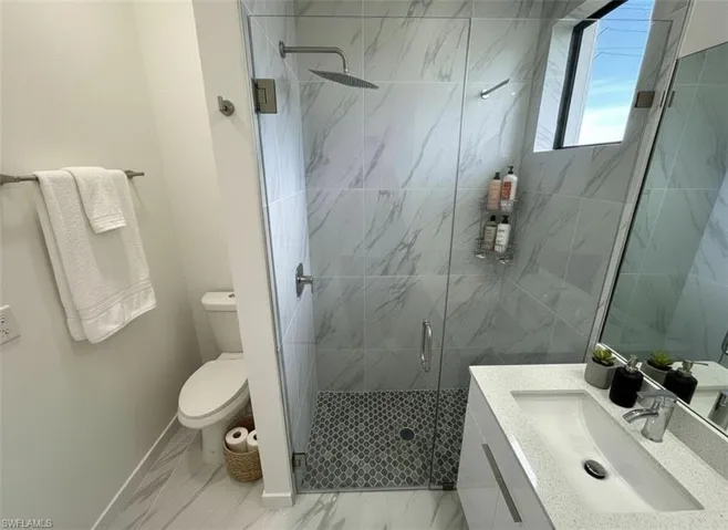 Full bath featuring vanity, a stall shower, and light marble finish floors