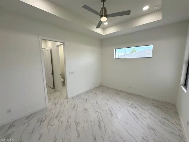 Unfurnished bedroom featuring a ceiling fan, a tray ceiling, recessed lighting, and light marble finish floors