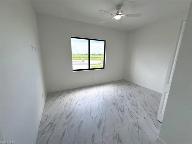 Unfurnished room featuring light marble finish flooring and a ceiling fan