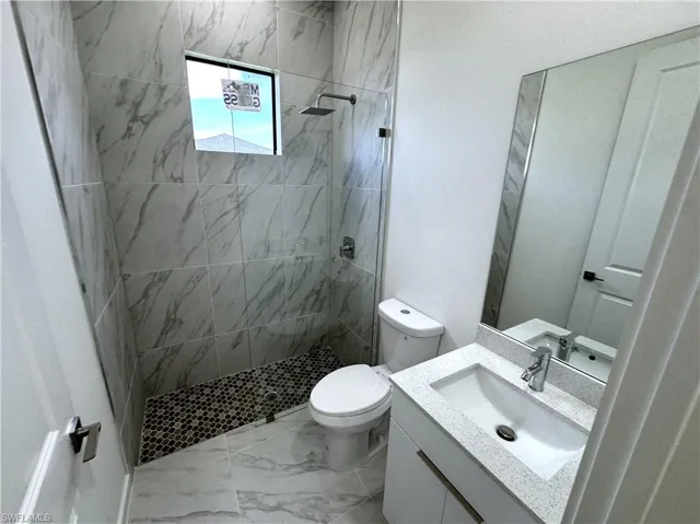 Full bath featuring vanity, a walk in shower, and light marble finish flooring