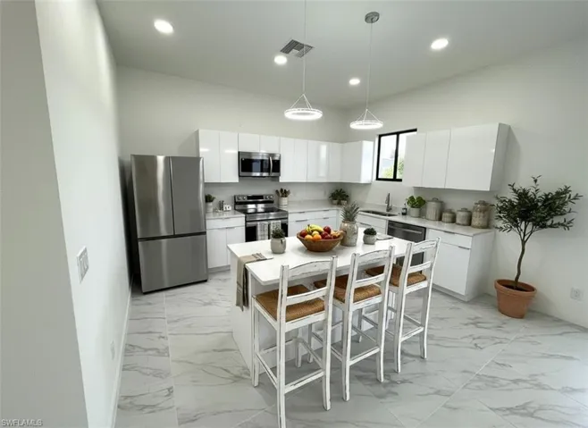 Kitchen with appliances with stainless steel finishes, pendant lighting, a kitchen breakfast bar, white cabinets, and recessed lighting