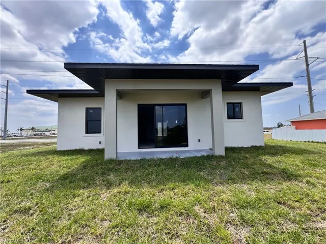 Back of house with stucco siding, a lawn, and a patio