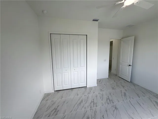 Unfurnished bedroom with a ceiling fan, a closet, and light marble finish floors