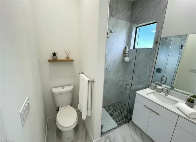 Full bathroom featuring a marble finish shower, vanity, and light marble finish flooring