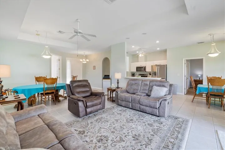 Living room featuring light tile patterned floors, ceiling fan, and a tray ceiling