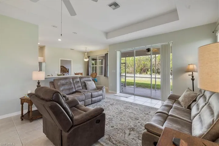 Living room with a raised ceiling, light tile patterned floors, and ceiling fan