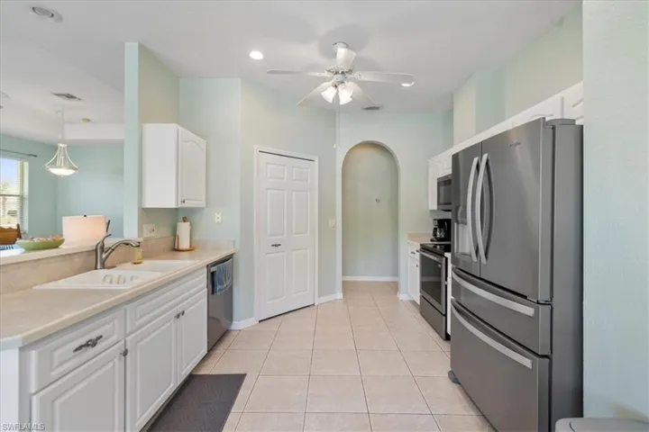 Kitchen featuring sink, light tile patterned floors, white cabinetry, stainless steel appliances, and decorative light fixtures